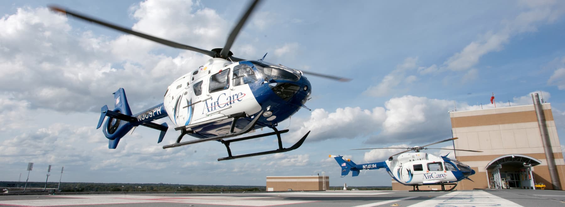 Two AirCare medical transport helicopters, one in the process of landing, on the heliport on top of the University Hospital.